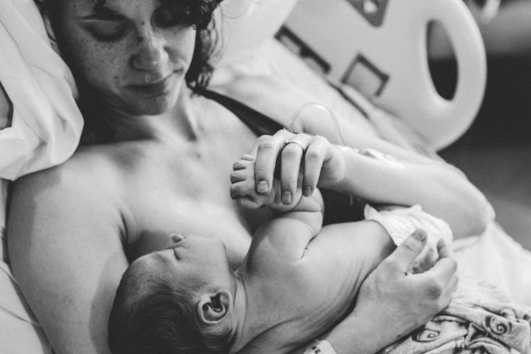 Black and white image capturing a tender moment between a mother and her newborn in a hospital setting.